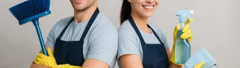 Uomo e donna collaboratori domestici sorridenti, schiena a schiena, con attrezzi per le pulizie in mano.