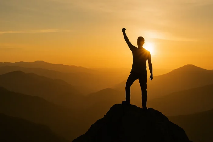 Silhouette di una persona che raggiunge la cima di una montagna al tramonto, simbolo della crescita personale e dell’essere allenabili.