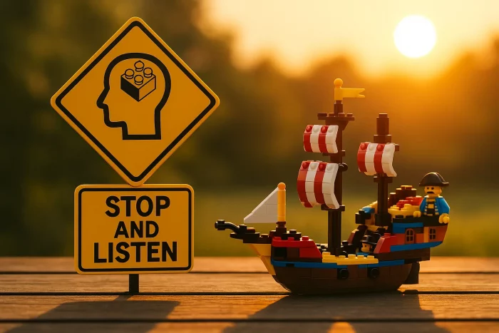 Cartello giallo “Stop and Listen” accanto a una nave LEGO illuminata dal tramonto, simbolo della pausa necessaria per ascoltare e ritrovare chiarezza.